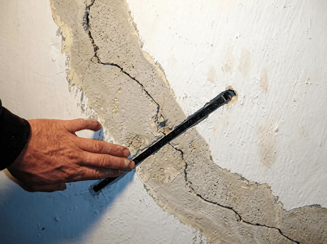 A wall with a large crack is being inspected by a professional in San Antonio, TX